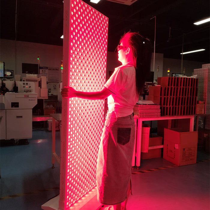 Woman standing in front of a full-body red light therapy panel in a clinic or lab setting